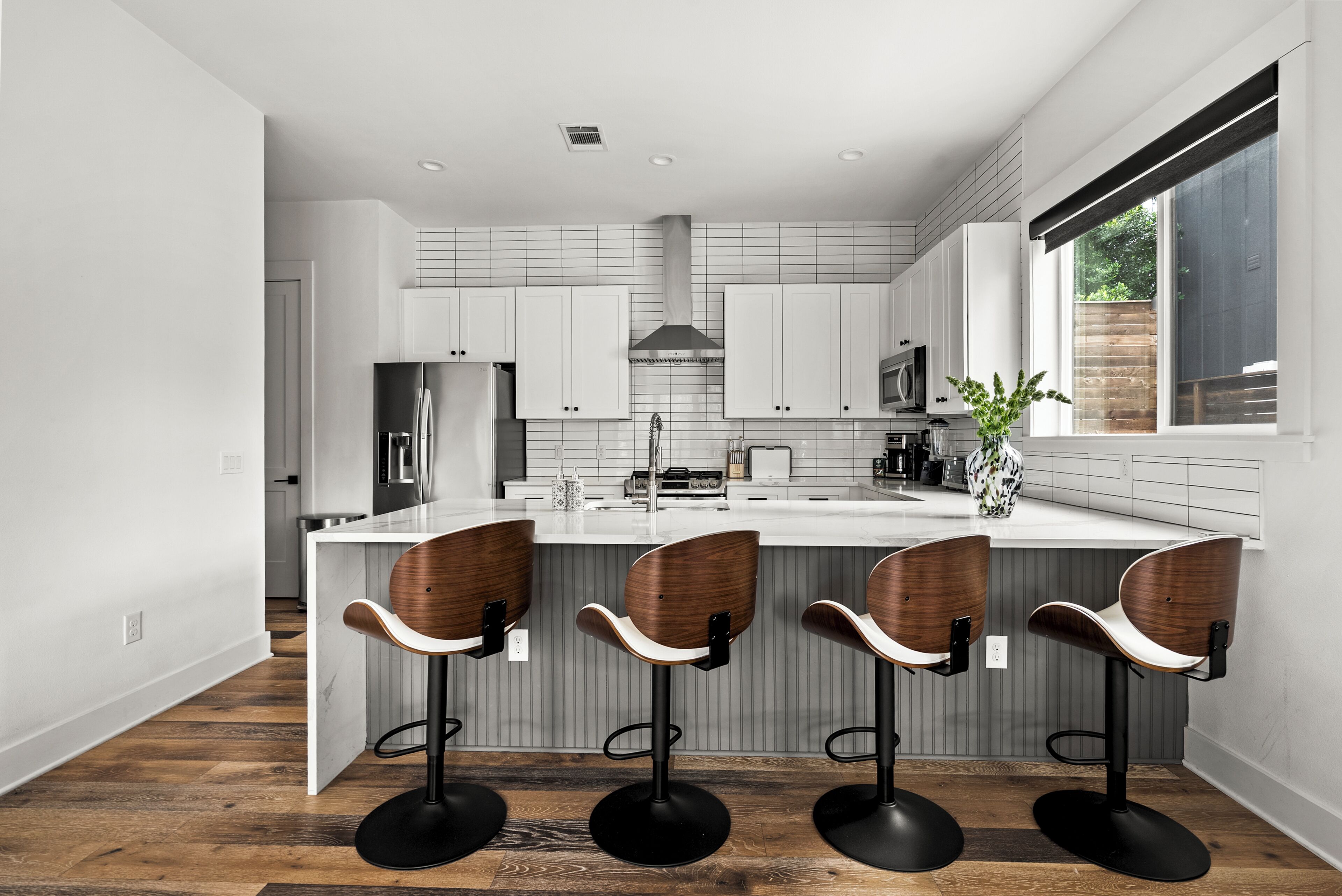 Een moderne keuken met een centraal eiland, barkrukken en een groot raam.