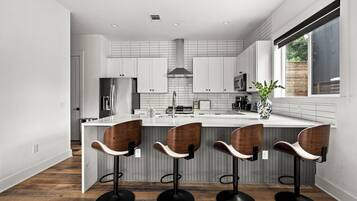 Een moderne keuken met een centraal eiland, barkrukken en een groot raam.