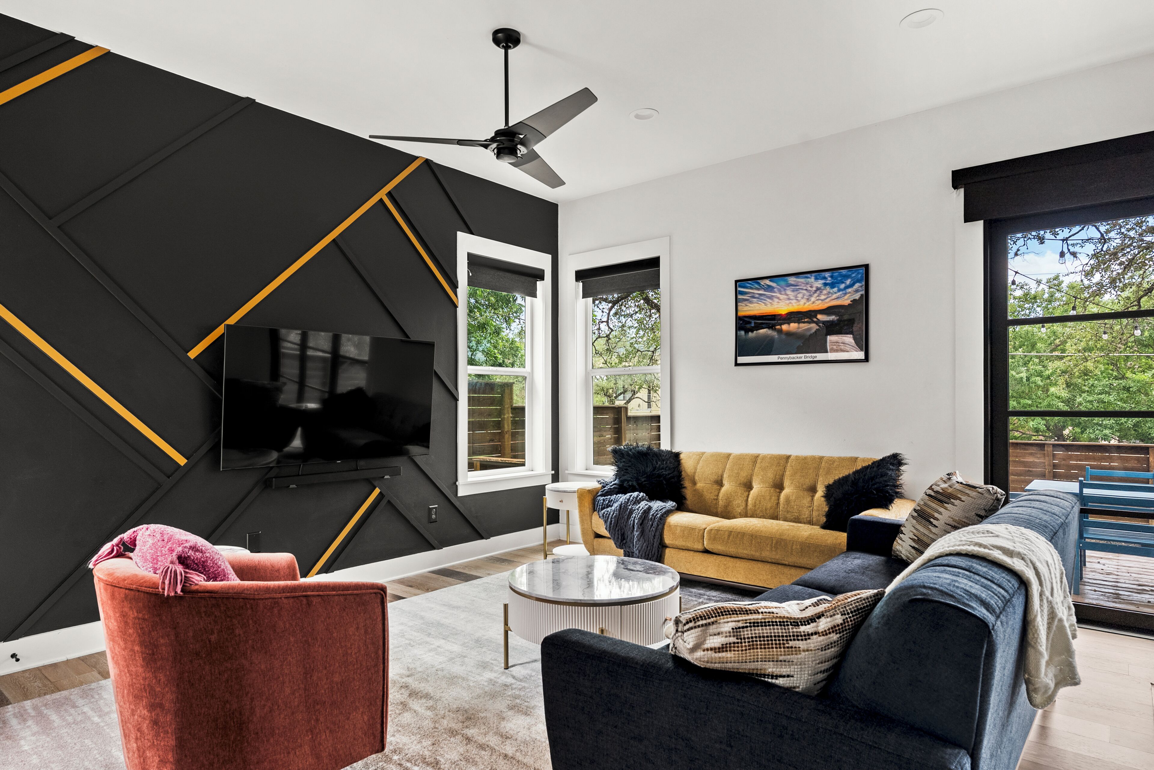 Ein modernes Wohnzimmer mit einem schwarz-gelben geometrischen Wanddesign, einer Couch, einem Fernseher und einem großen Fenster.