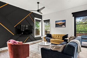 A modern living room with a black and yellow geometric wall design, a sofa, a television, and a large window. - South Austin Luxury: SoCo, S. 1st + Cowboy Pool (Austin)