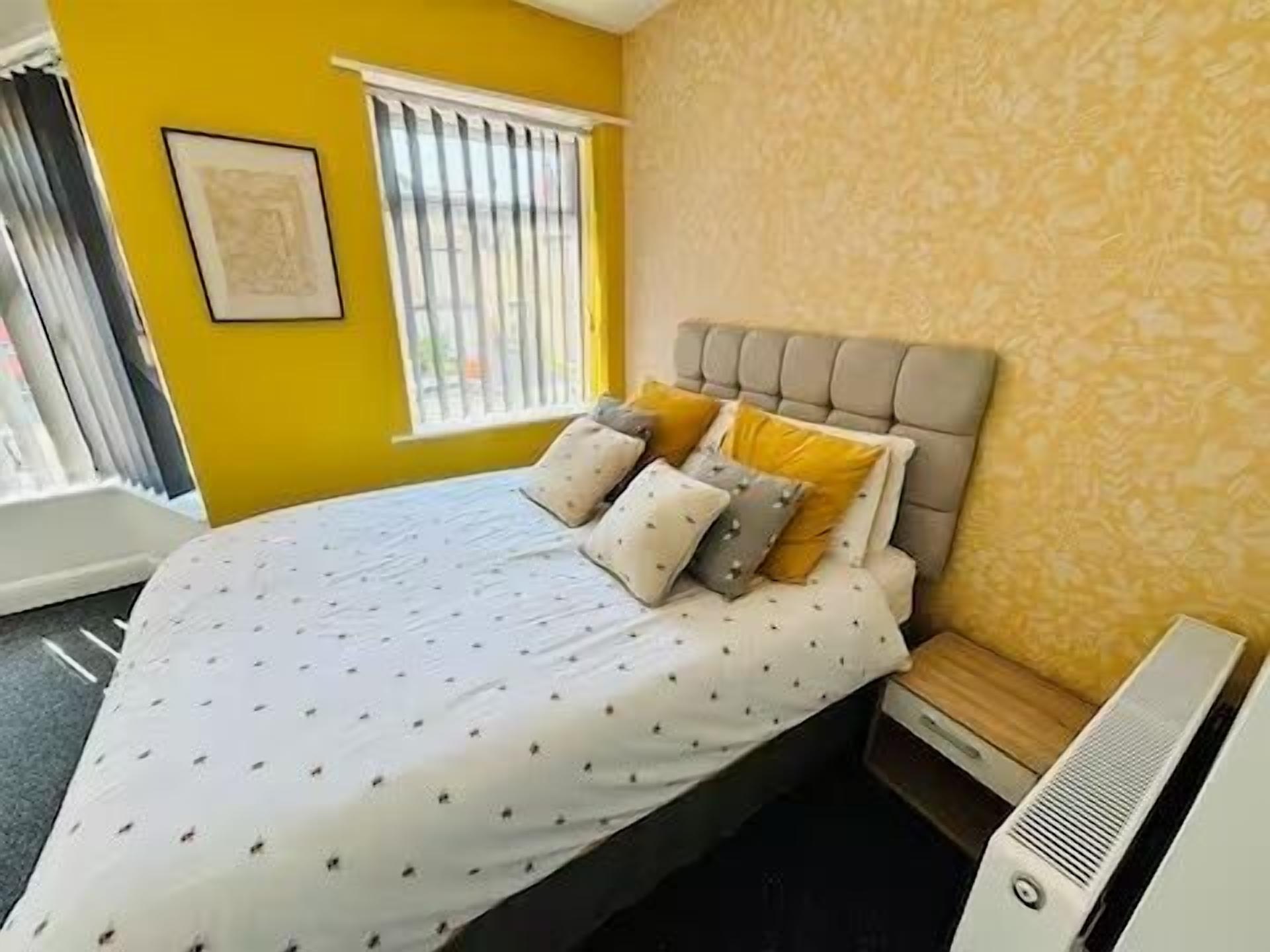 A bedroom with a bed, a window with blinds, a radiator, and a wall-mounted picture.