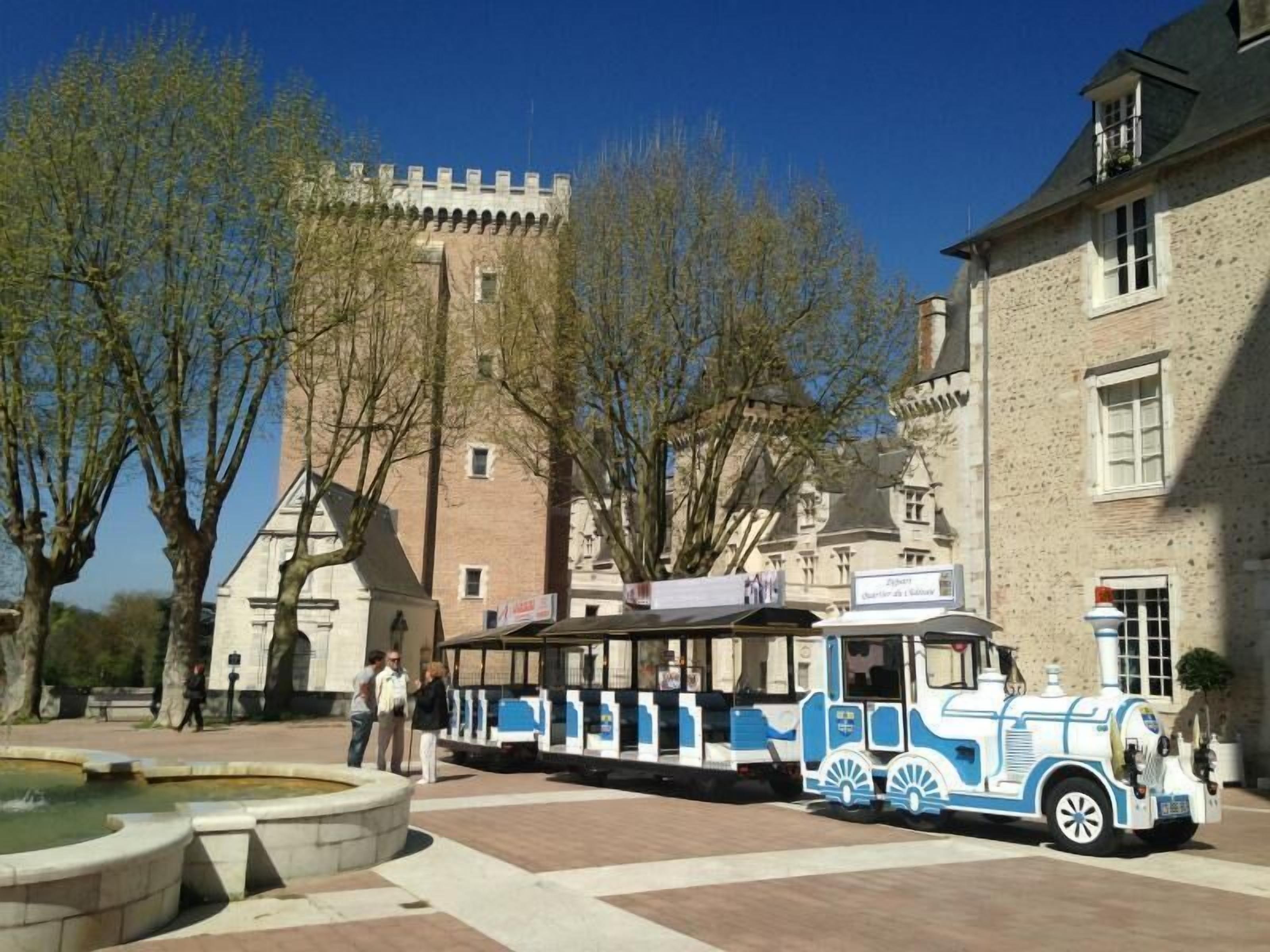Un tramway de style rétro se trouve sur une place publique, avec un château en arrière-plan.