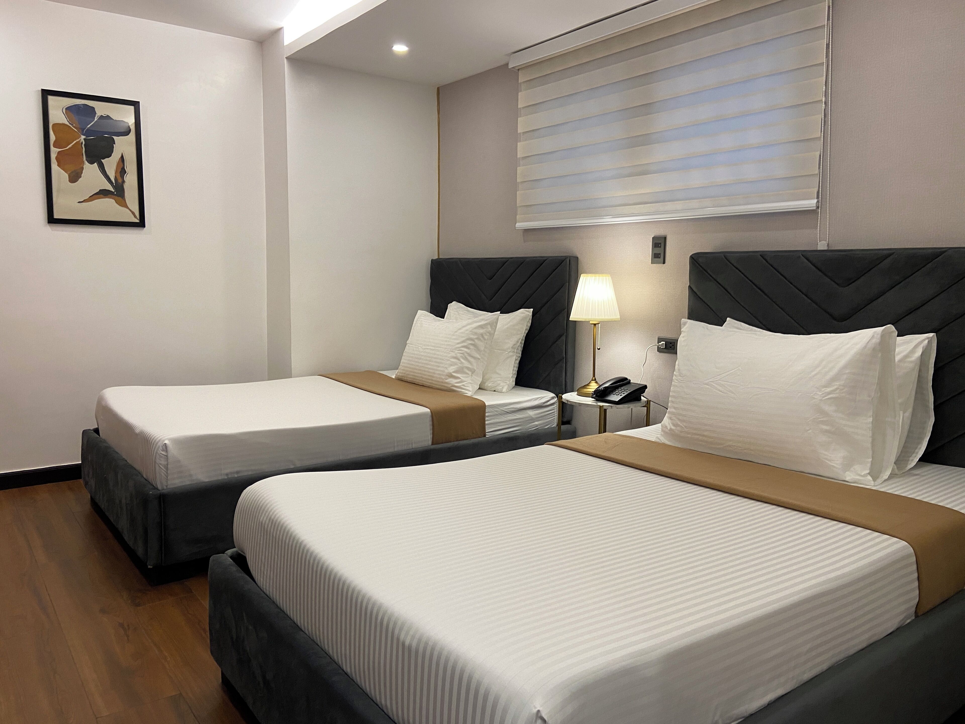 A hotel room with two beds, a bedside table with a lamp, and a wall-mounted painting.