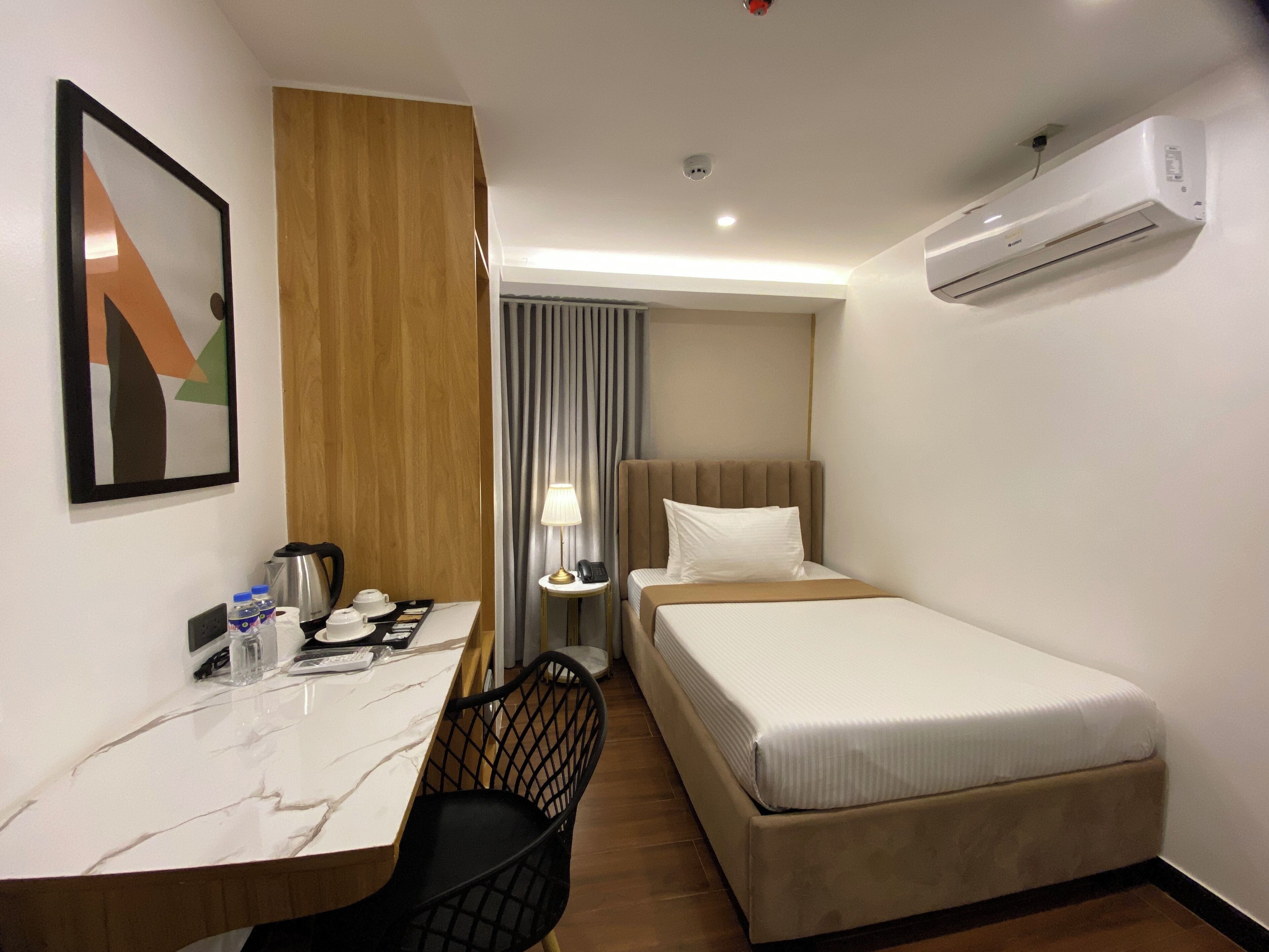 A hotel room with a single bed, a desk with a chair, a lamp, a telephone, and a water dispenser.