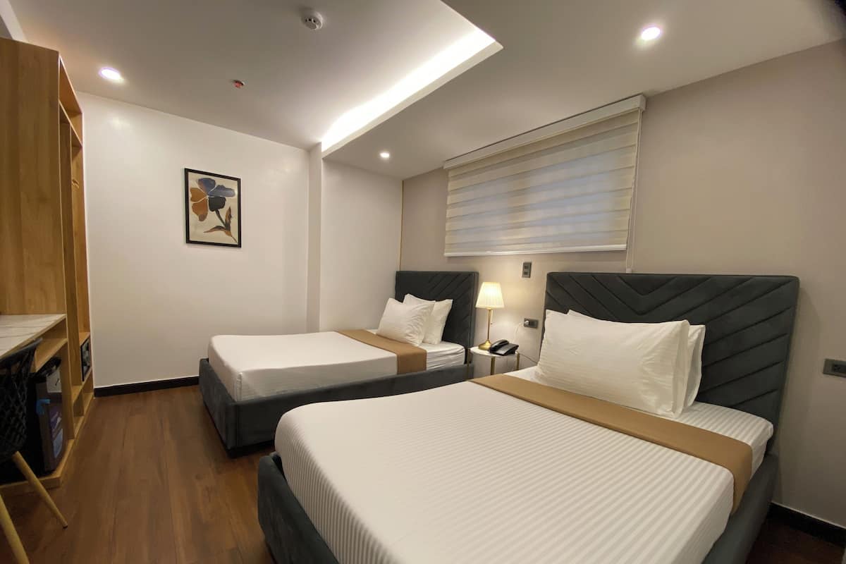 Habitación de hotel con dos camas, un escritorio, una lámpara y un cuadro en la pared.