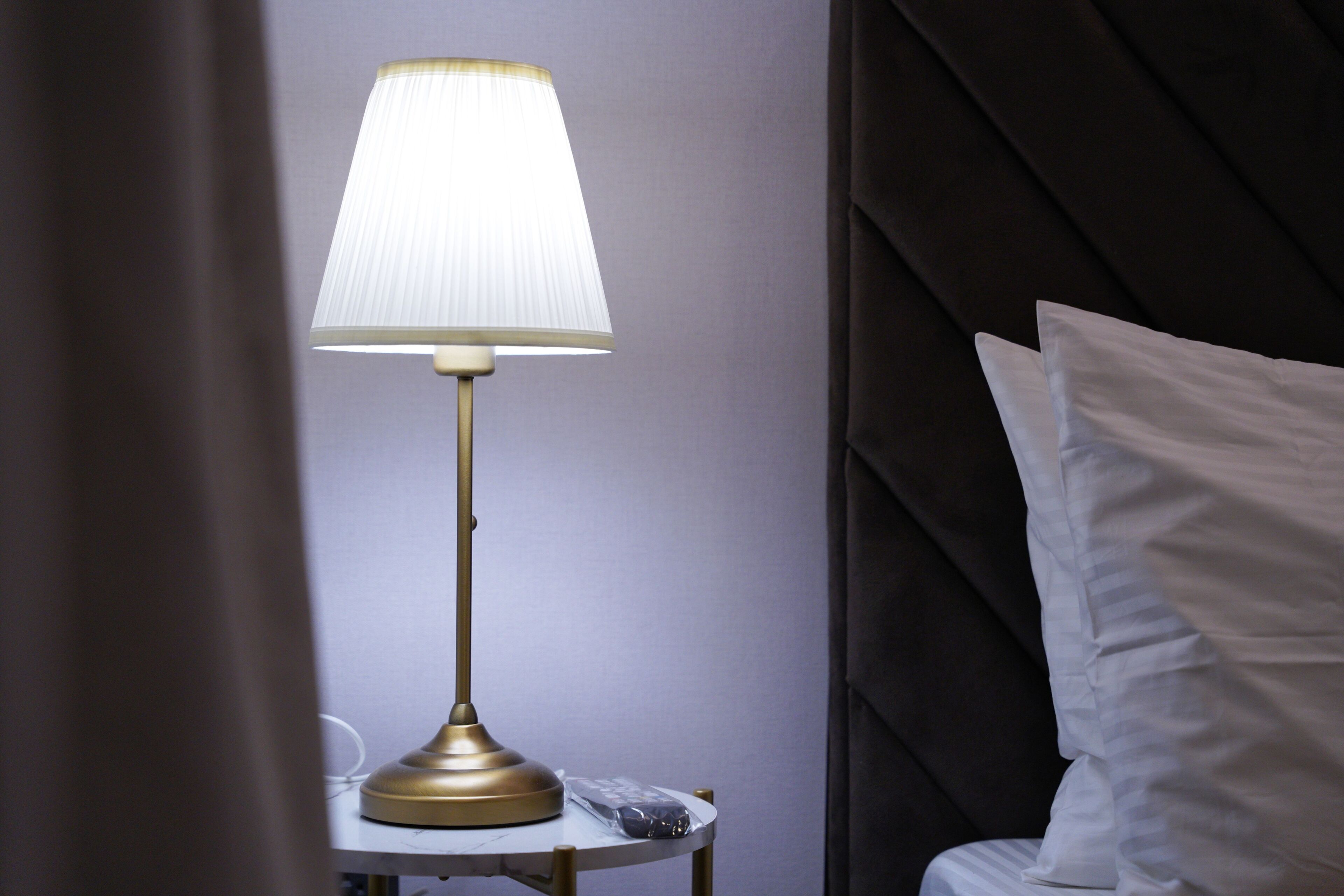 Une table de chevet avec une lampe, un oreiller et un petit objet posé dessus.