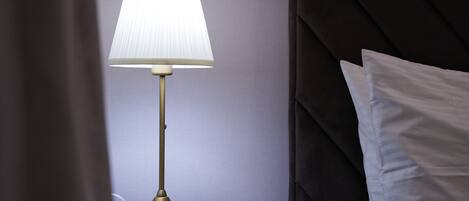 A bedside table with a lamp, a pillow, and a small object on the table.