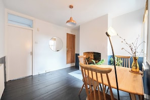 A room with a wooden dining table, chairs, a round mirror, and a hanging pendant light.