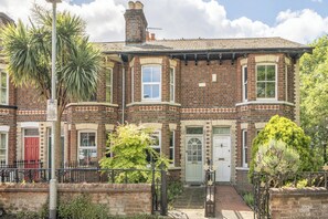 A Victorian-style brick house with a bay window, a red door, and a small garden with a palm tree. - Victorian Terrace near Uni, sleeps 6, Garden (Reading)