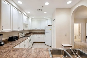 A kitchen with white cabinets, a microwave, a refrigerator, a stove, and a sink. - Sunlit Escape Resort Stay (Kissimmee)