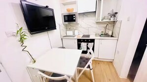 Une cuisine compacte comprenant une table à manger, des meubles blancs, un four à micro-ondes et un téléviseur fixé au mur.