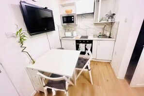 A compact kitchen with a dining table, white cabinets, a microwave, and a TV mounted on the wall. - Studio Sleeps 2 with Shared Hot Tub (London)