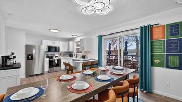A modern kitchen with white cabinets, a dining area with a wooden table set for four, and a large window with curtains.