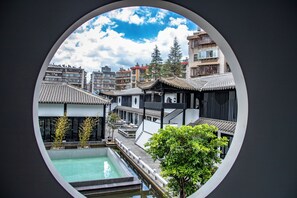 A courtyard with a swimming pool, traditional buildings, and a view through a circular window. - Gongxili - Xijian Hotel (Kunming)