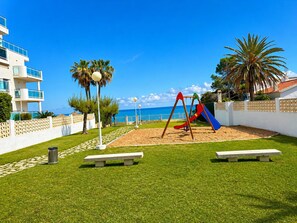 Ein Spielplatz mit Rutsche und Schaukeln, einer Bank und Blick aufs Meer.