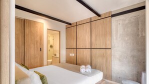 Een moderne slaapkamer met een groot bed, een houten garderobe en een klein rond tafeltje.