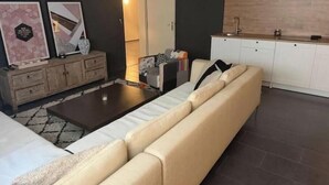 Un salon comprenant un canapé, une table basse, un meuble et un coin cuisine avec des placards et un plan de travail.