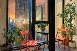 A balcony with two red chairs, a small round table, and potted plants. - Modern City Gem 3BR | Pool, Gym and 2 Free Parking (Southbank)