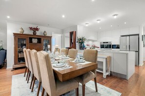 A modern kitchen with stainless steel appliances, a dining area with a wooden table and chairs, and a decorative cabinet with glass doors. - Triple Aspect Views - from the City to the Sea (Southbank)