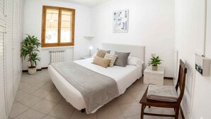 A bedroom with a bed, bedside tables, a chair, a window, and a radiator. - Holiday apartment mit Klimaanlage und Balkon (Imperia)