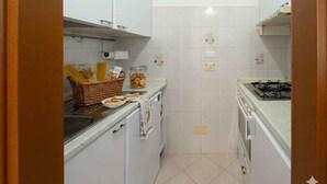 A compact kitchen with white cabinets, a gas stove, and a countertop with a basket of bread and a jar of cookies. - Holiday apartment mit Klimaanlage und Balkon (Imperia)