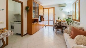 A living room with a sofa, a dining table with chairs, a kitchen area with cabinets, and a sliding glass door leading to a balcony. - Holiday apartment mit Klimaanlage und Balkon (Imperia)