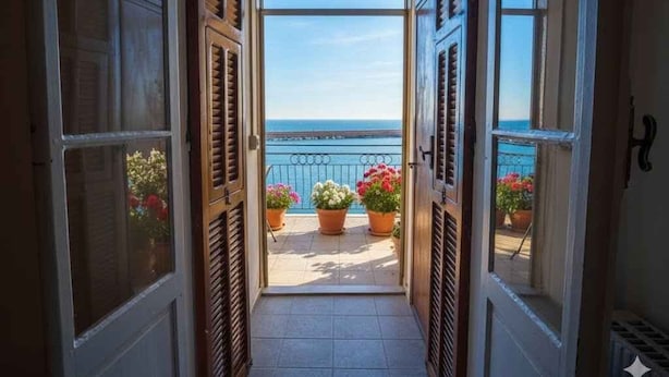 Ein Korridor führt zu einem Balkon mit Topfpflanzen und Blick aufs Meer.