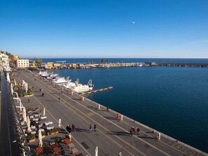 Eine Uferpromenade mit vor Anker liegenden Booten und einem Steg, der sich ins Wasser erstreckt, unter blauem Himmel.