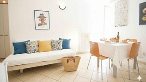 Una habitación con una cama, una mesa de comedor con sillas, una cesta y un cuadro colgado en la pared.