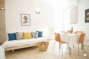 A room with a bed, a dining table with chairs, a basket, and a wall-mounted picture. - Holiday apartment mit Klimaanlage und Balkon (Imperia)