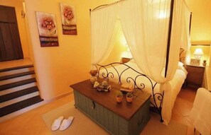 A bedroom with a bed, a nightstand, a bedside table, a window with curtains, a small table with decorative items, and a pair of slippers on the floor. - Holiday apartment with balcony and internet (Imperia)