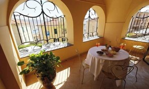 A round table with a white tablecloth, surrounded by metal chairs, in a room with arched windows and a potted plant. - Holiday apartment with balcony and internet (Imperia)