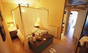 A bedroom with a four-poster bed, a bedside table with a lamp, a radiator, and a view of a hallway. - Holiday apartment with balcony and internet (Imperia)