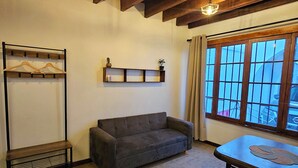 A room with a wooden ceiling, a grey sofa, a table with a placemat, a hanging light fixture, and a window with bars. - Forest Hostel B&B (Santiago)