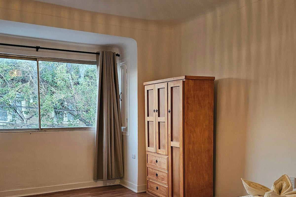 A bedroom with a large bed, a wardrobe, a window with curtains, and a hanging light fixture.