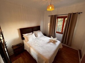 A neatly made bed with a white bedspread and pillows, a wooden headboard, a bedside table with a remote control, and a hanging light fixture. - Wanderlust Hostel B&B (Santiago)