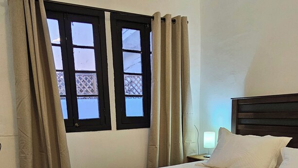 A hotel room with a bed, curtains, a window, and a bedside lamp. - Forest Hostel B&B (Santiago)