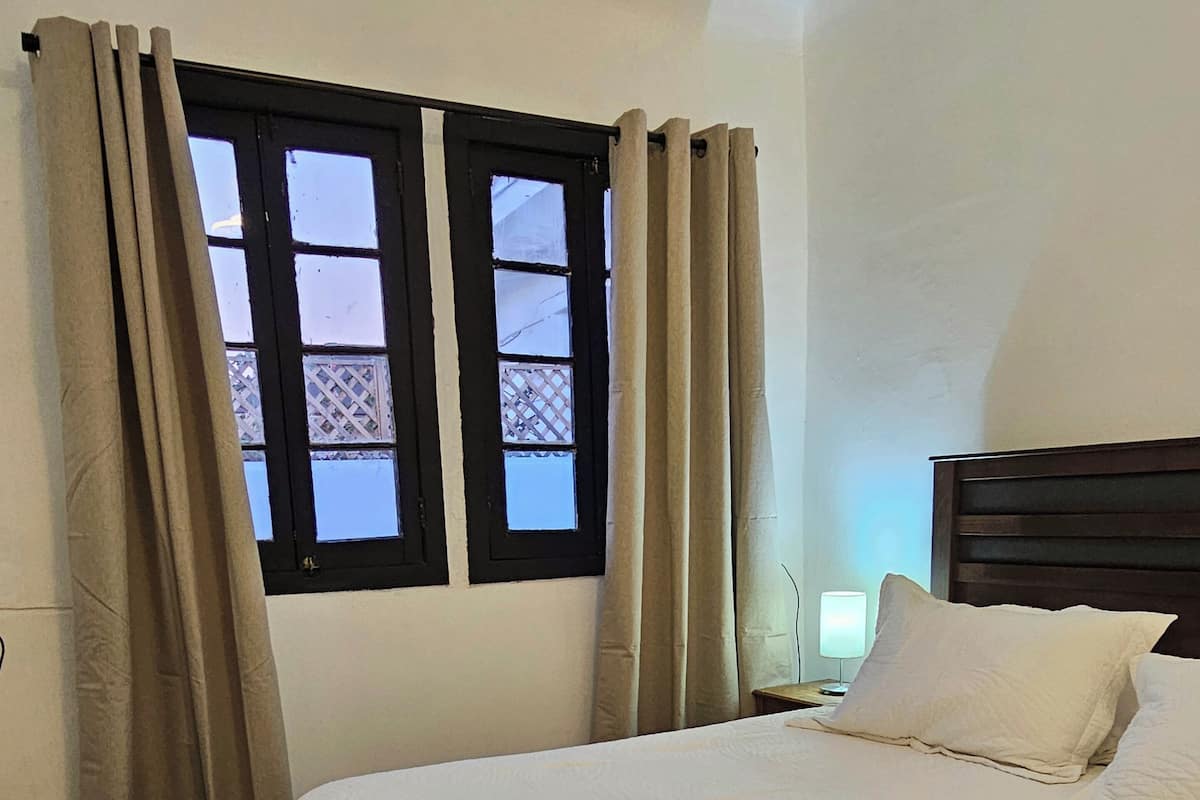 A hotel room with a bed, curtains, a window, and a bedside lamp.