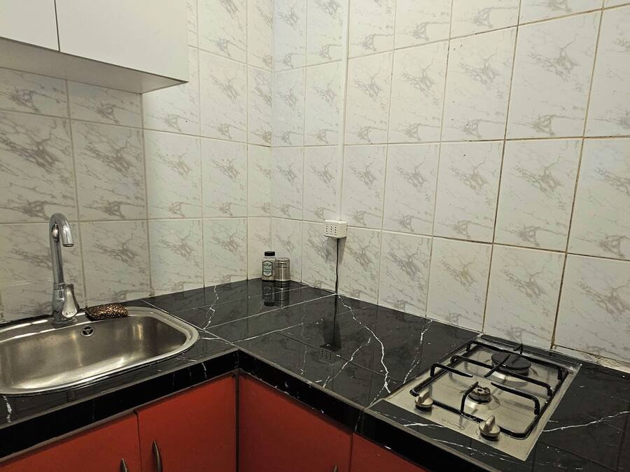 A kitchen with a sink, stove, cabinets, and marble-patterned tiles.