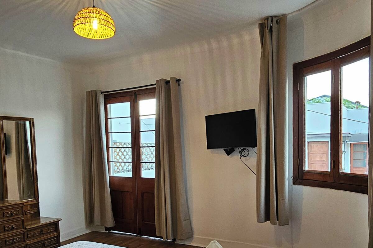 A hotel room with a bed, a television, a window with curtains, and a ceiling light fixture.