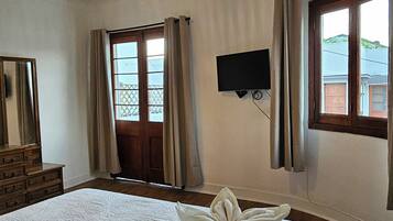 Habitación de hotel con cama, televisión, ventana con cortinas y lámpara en el techo.