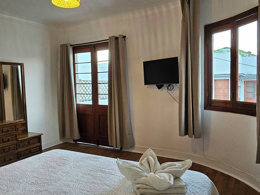 Habitación de hotel con cama, televisión, ventana con cortinas y lámpara en el techo.