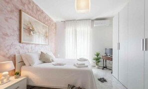 A bedroom with a bed, bedside table, lamp, and a desk with a chair. - Holiday apartment mit Klimaanlage und Balkon (Imperia)