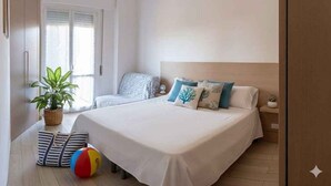 Un dormitorio con cama, mesita de noche, lámpara, planta en maceta y una pelota de playa.