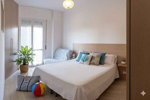 A bedroom with a bed, bedside table, lamp, potted plant, and a beach ball. - Holiday apartment with air conditioning and balcony with sea view (Diano Marina)
