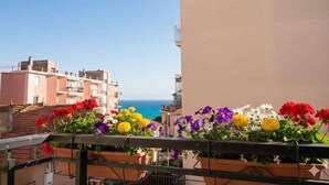 Un balcón con macetas de flores, vistas despejadas al mar y edificios al fondo.