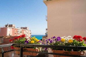 A balcony with potted flowers, a clear view of the sea, and buildings in the background. - Holiday apartment with air conditioning and balcony with sea view (Diano Marina)