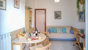 Una sala de estar acogedora con un sofá, una mesa de comedor con una cesta de pan y una botella de vino.