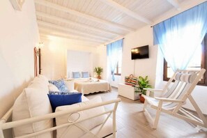 Ein Zimmer mit einem weißen Sofa, einem gestreiften Sessel, einem Fernseher und einem Fenster mit Vorhängen.