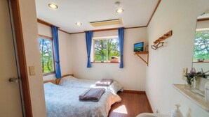 A bedroom with two beds, a TV, a window with curtains, a mirror, and a bathroom with a sink and toiletries.